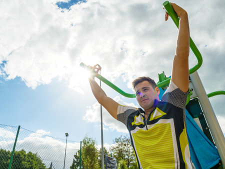 Man exercises on the public gym equipment in open air. Sporty guy flexing his muscles on machine. Staying fit and healthy.の写真素材