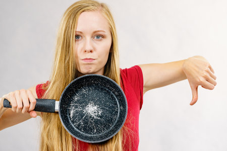 Woman holding scratched frying pan. Torn coating, kitchen utensils is unusableの写真素材