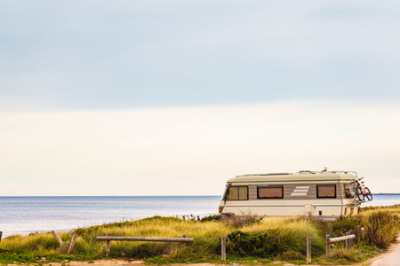 Camping on sea shore. Old caravan vehicle on beach, mediterranean coast in Spain.の写真素材