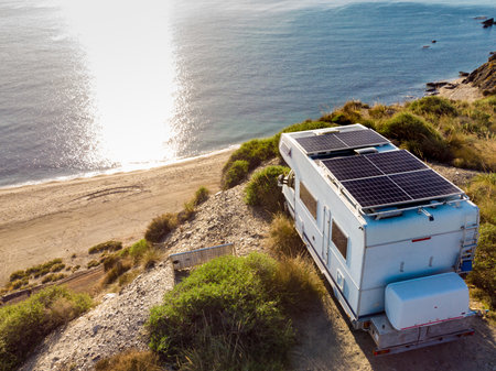 Aerial view. Caravan with solar photovoltaic panels on roof camping on cliff sea coast....