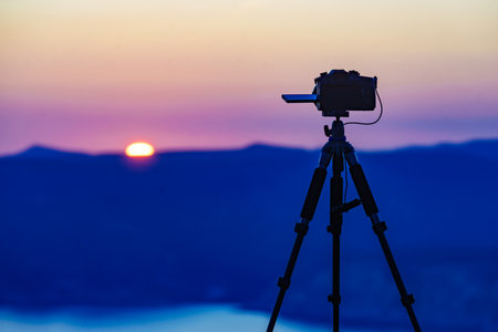 Professional camera on tripod taking photos film video of sunset over sea coast