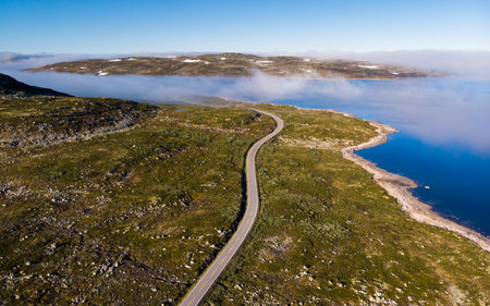 Aerial view. Road crossing Hardangervidda mountain plateau, clouds over lakes, morning time. Norway landscape. National tourist Hardangervidda route.の写真素材