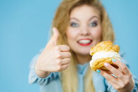 Sweet food and happiness concept. Funny joyful blonde woman holding yummy choux puff cake with...