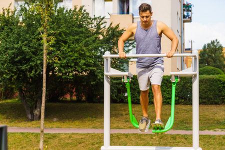 Young man working out in outdoor gym, doing legs exercises on public machine in park. Staying fit...