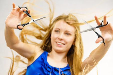 Haircut coiffure haircare concept. Girl with blowing long blond hair holding scissors, showing work...