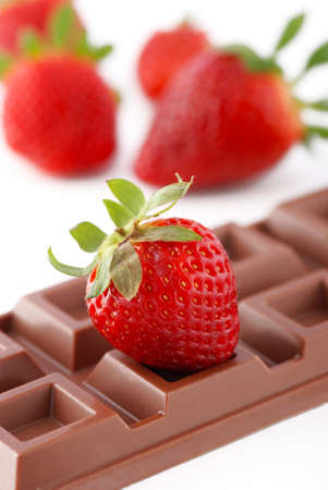 strawberry resting on the bar of chocolate with fruit in the backgroundの写真素材