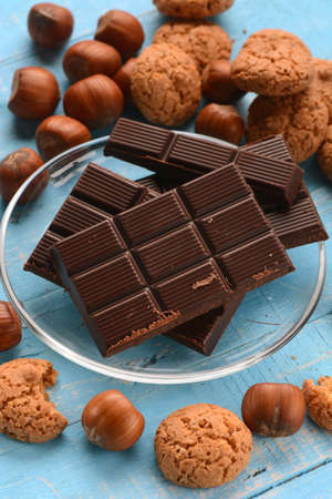 Chocolate tablet on glass dish with hazelnuts and biscuits around