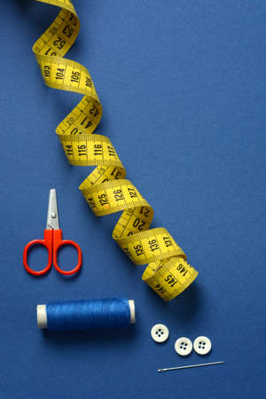 sewing utensils on blue background - tape measure, scissors, cotton thread - closeup