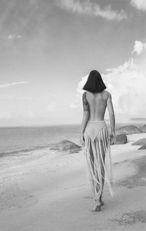 Back view of a beautiful young woman with long black hair standing on the beach and looking awayの写真素材