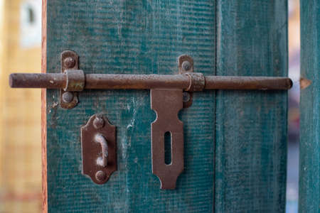 A close up photo of a brown vintage and rusty iron latch in the old gate of a house