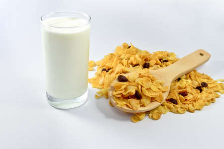 Cornflakes with currant in a wooden spoon and a glass of milk on white background