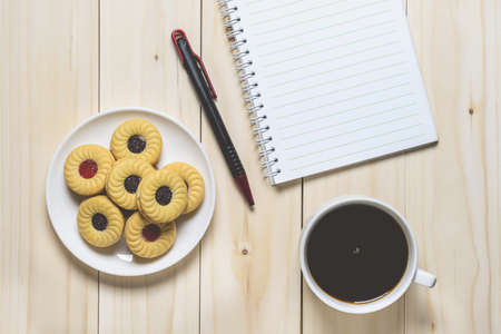 Cup of coffee, biscuits and a blank open notebook on wooden background. flat layの写真素材