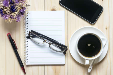 Flat lay desk with coffee, notebook, smartphone, eyeglasses and flowersの写真素材