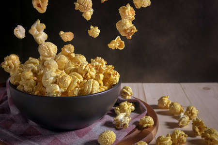 Caramel covered popcorn in black ceramic bowl on wooden table,  levitation popcorn and mystic photographyの写真素材