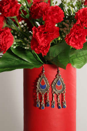 Beautiful set of flowers and handmade earrings hanging on a red vase.の写真素材