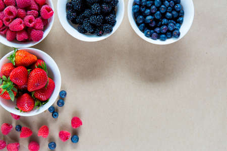 Small white bowls filled with ripe strawberries, raspberries, blueberries  and blackberries, copy space, top view. Healthy nutrition conceptの写真素材