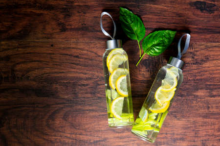 Two Glass bottles of water with lemon decorated with mint leaves on wooden background.の写真素材