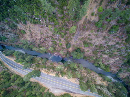 Aerial view of Mountain road with forested hills, fire burned dead trees along a narrow river.
