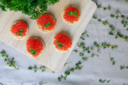 Delicious canapes. Closeup of red caviar appetizer served on crackers and decorated with green...