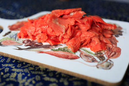 Close up of thinly sliced smoked salmon on a wooden cutting board with seafood pattern.