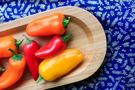 Fresh organic sweet peppers on a wooden plate on background table.の写真素材