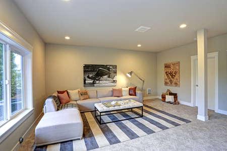 Light entertainment/game room design in a luxury new construction home showcases soft beige sectional with red pillows offering comfortable seating atop a white and blue striped rug.の写真素材