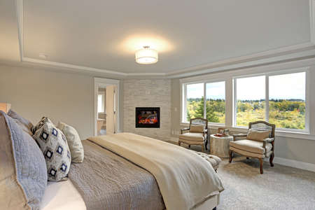 Luxury master bedroom interior with large bed, stone fireplace and a pair of comfortable reading chairs.の写真素材