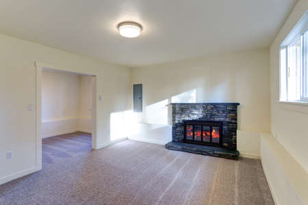 Light empty living room interior with milky walls framing a wall mounted fireplace with natural stone tile sorround. 