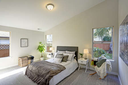 Cozy bedroom interior with vaulted ceiling, a white bed with a grey headboard and a grey velvet...