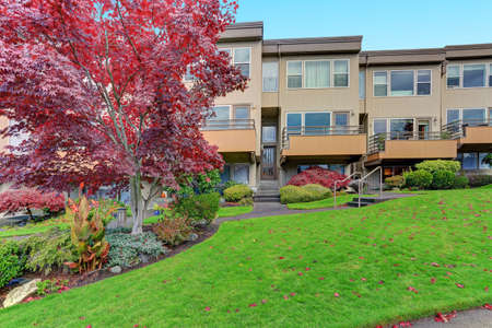 Condominium, apartment building with beige siding, three floors, private balconies, green grass and neatly trimmed shrubs in front.
の写真素材
