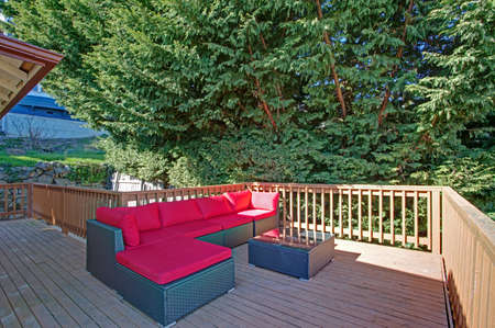 Second floor deck features wicker outdoor sofa with red cushions.