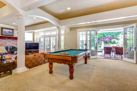 Spacious game room with white columns, billiard table and exit to outdoor patio.