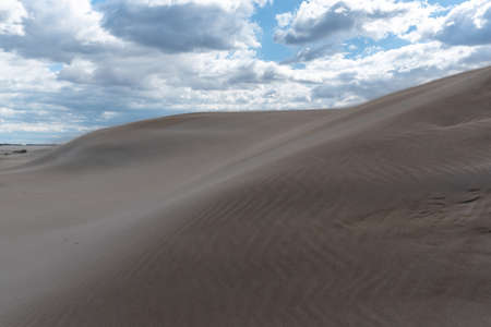 Sand forming dunes in the middle of the desert with a sky with clouds. Brown, blue and gray colorsの写真素材
