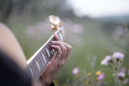 Person playing music with acoustic guitar in the middle of the field, surrounded by green plants and...