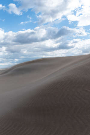 Sand forming dunes in the middle of the desert with a sky with clouds. Brown, blue and gray colorsの写真素材