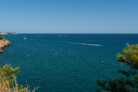 View of the beautiful blue Mediterranean sea with rocks near the shore with waves on a sunny day with boats and sailboatsの写真素材