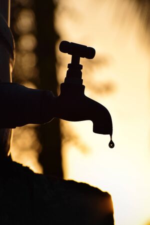 vertical / portrait oriented , Silhouette of old vintage metal tap leaking water droplet . Alone in outdoor natural environment during golden hour , wallpaperの写真素材