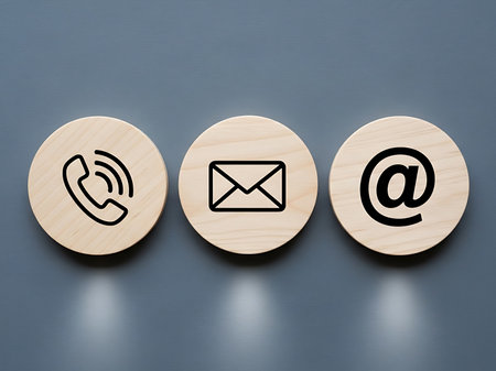 Three light wood circles with black line icons for phone, email, and at symbol on a solid blue background.の素材