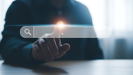 A person's hand and finger are touching a glowing digital search bar interface with a magnifying glass icon.の素材