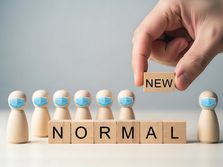 A hand places a wooden block with the word NEW above wooden figures wearing blue face masks and blocks spelling NORMAL.の素材