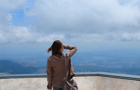 Young woman standing on cliff s edge and looking to a sky with raised hands 