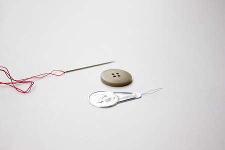 needle,threader and button against white background