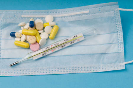 Pills, thermometer, medical face mask, on a blue background. care during illness concept