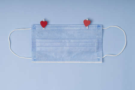 Concept of love in new normal reality. Protective medical mask with wooden clothespins with hearts...
