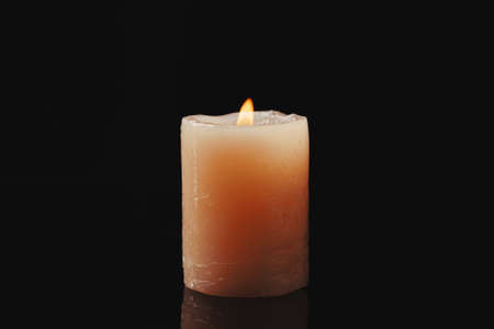 single candle light glowing on an yellow candle on black backgroundの写真素材