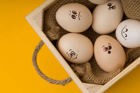 wooden Basket with funny eggs with painted faces on an yellow backgroundの写真素材