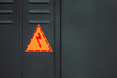 yellow triangle with lightning on a fence made of metal mesh.