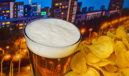 foamy beer in a glass with potato chips