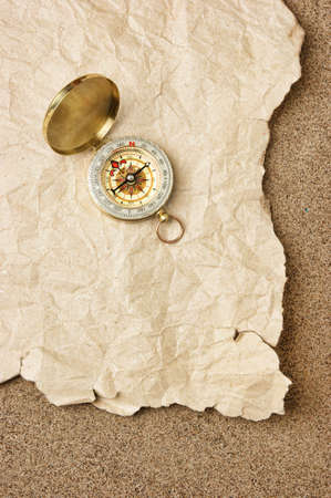 Compass on old sheet crumpled paper against the background of sandの写真素材