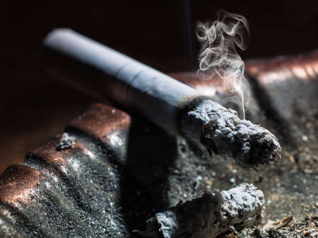 Closeup of cigarette on ashtray with a beautiful wisp of smoke on a dark backgroundの写真素材